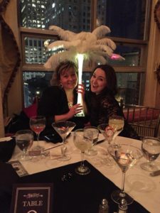 Two women sitting at a table with wine glasses and a feather lamp.