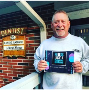 A man holding up a book outside of a dentist office.