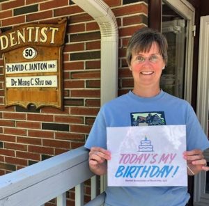 A woman holding up a sign in front of a dentist office.