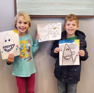 Two children holding up drawings of a shark.