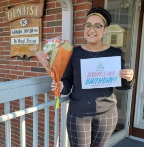 A woman holding a sign and flowers outside of a dentist office.