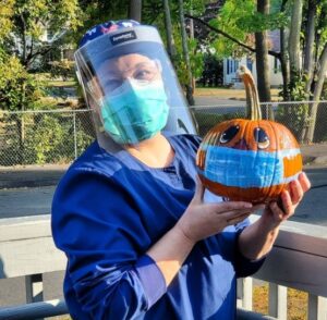 A person holding an orange pumpkin wearing a face shield.