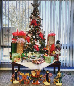 A table with presents and christmas tree in front of windows.
