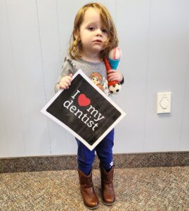 A little girl holding up a sign with the words " i love my dentist ".